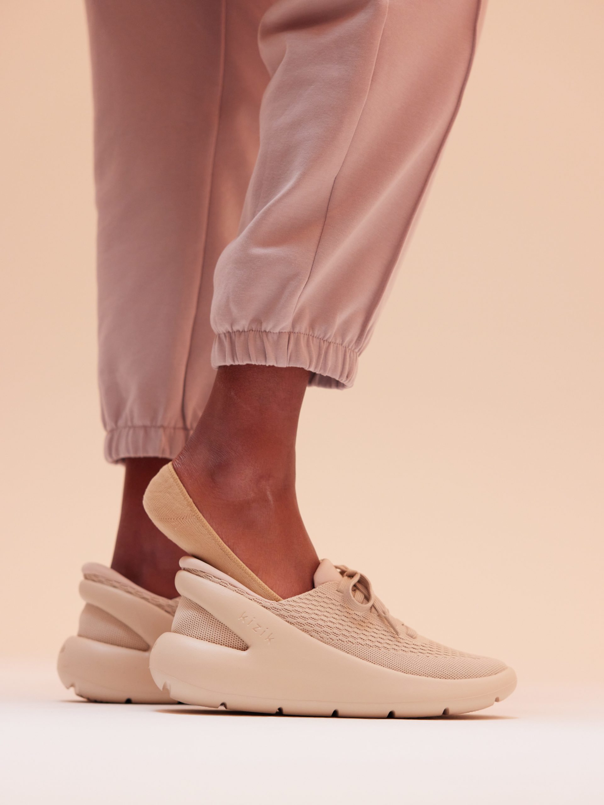 Visual of a woman stepping into Kizik's newest athleisure sneaker, Roamer, in pink.
