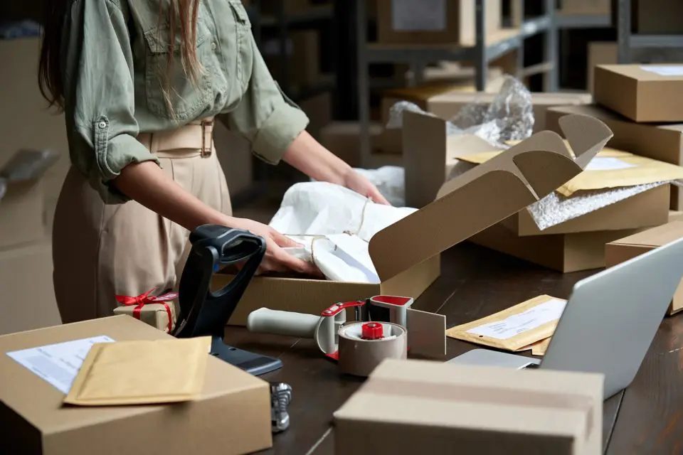 A woman standing at a desk packing a box with products to be returned after Amazon Prime Day 2023.